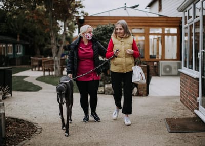 A woman walking with a resident and a dog outdoors.