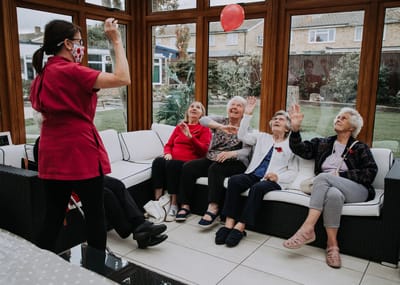 Residents and staff play with a balloon in a common area.