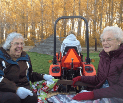 Two women enjoying time outdoors with a tractor in the background.