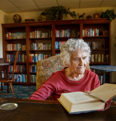 An elderly woman reading a book in a cozy library