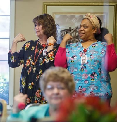 Two staff members flexing muscles with a resident in the foreground