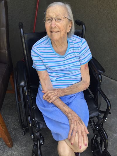 Smiling elderly woman in a wheelchair outdoors.
