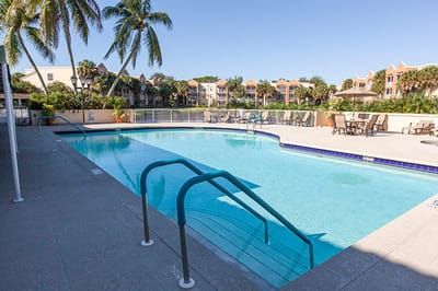 Outdoor pool area surrounded by palm trees and buildings