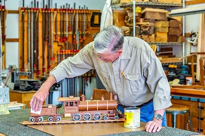 A resident working on a wooden train model in a workshop