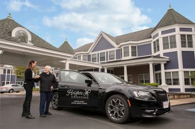 Resident and staff interacting near facility entrance and vehicle