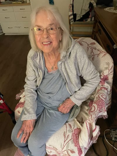 An elderly woman smiling in a cozy chair