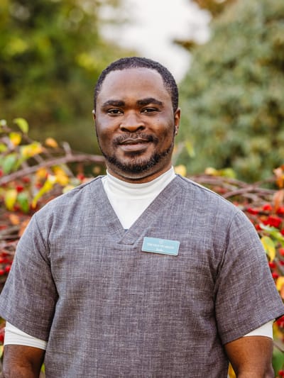 Staff member smiling outdoors in front of foliage.