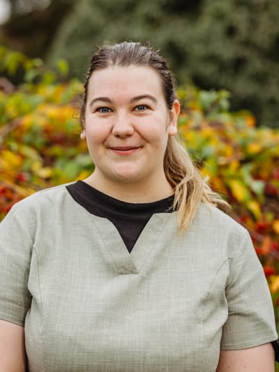 Staff member smiling outdoors among colorful foliage.
