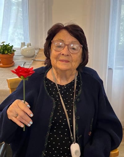 Senior resident holding a red flower indoors.