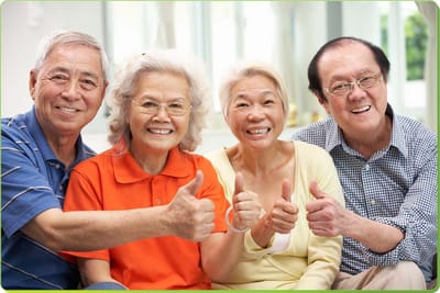 Four seniors smiling and giving thumbs up indoors.