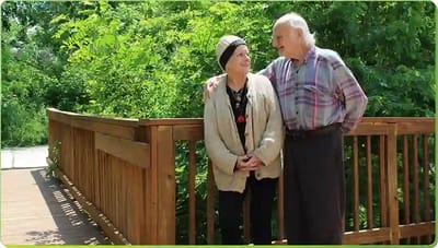 Two seniors sharing a moment on a wooden bridge.