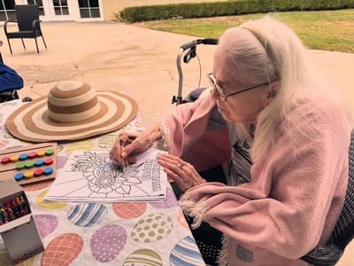 Elderly woman coloring outdoors at a table.