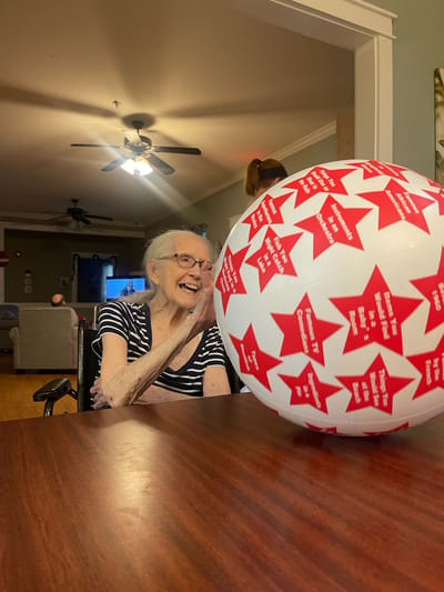Elderly woman engaging with a colorful ball indoors.
