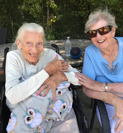 Two elderly women smiling outdoors.