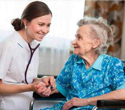 A caregiver smiling and holding the hand of an elderly resident in a bright room.