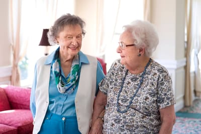 Two elderly women smiling and conversing in a common area