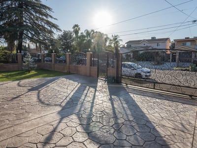 Sunlit entrance with decorative wrought-iron gate and stone pathway.