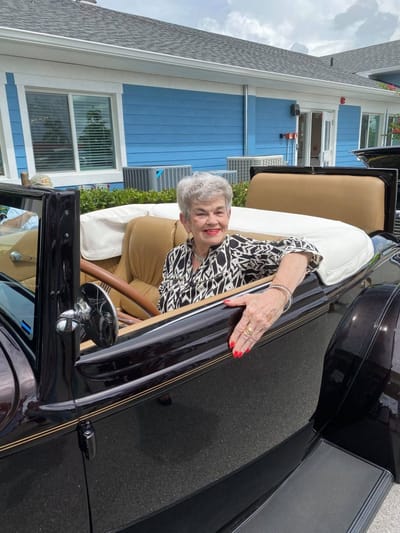 Senior resident enjoying a ride in a vintage car outside the facility