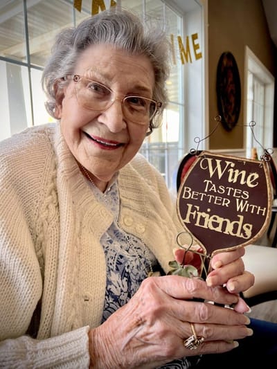 Resident holding a sign that says 'Wine Tastes Better With Friends'