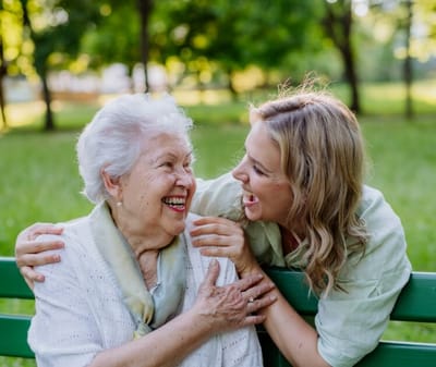 A senior woman and a caregiver laughing together outdoors