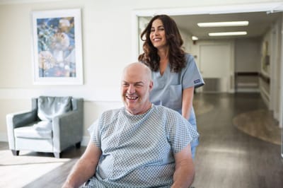 A resident smiling with staff assistance in a hallway
