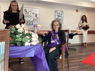 A resident celebrating with staff and flowers in a common area
