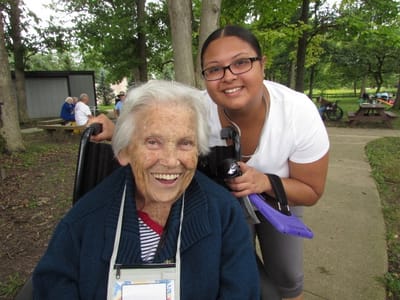 Smiling resident in a wheelchair with staff outdoors