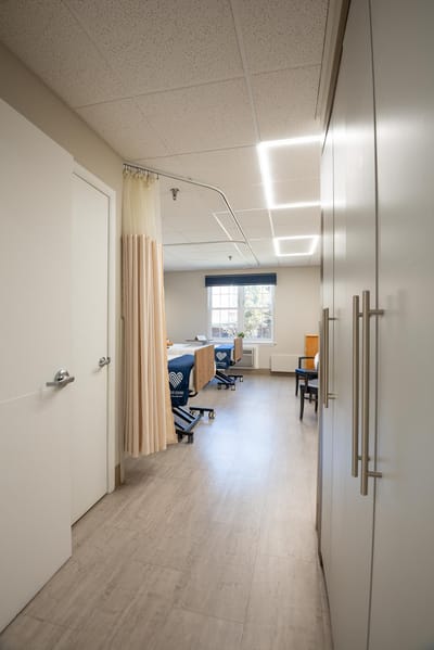 A well-lit nursing facility room with a bed and sitting area