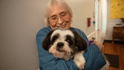 A resident happily holding a small dog indoors