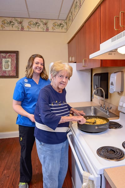 A resident cooking with a staff member in a kitchen