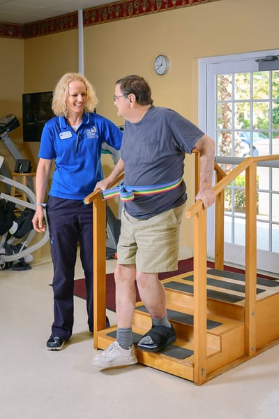 Staff assisting a resident with stairs in therapy area
