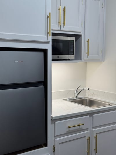 A kitchenette with a refrigerator and microwave in a senior living unit