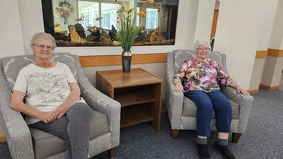 Two residents sitting in comfortable chairs with a fish tank behind them