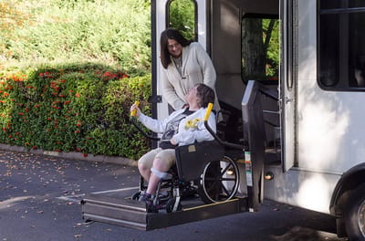 Resident using wheelchair lift with staff assistance.