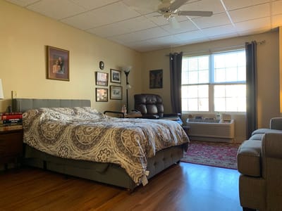 Well-lit private resident room with a bed and seating area