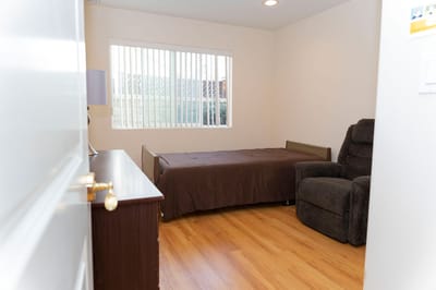 A well-furnished private resident room with a bed and recliner