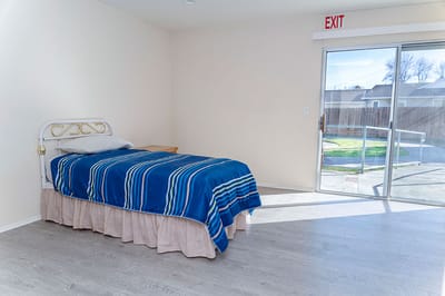 Brightly lit resident room with a bed and exit door