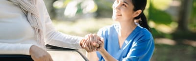 Caregiver and senior holding hands outdoors.