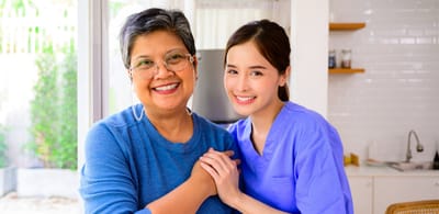 A smiling elderly woman with a caregiver in a bright room.