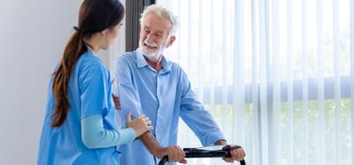 A caregiver assisting a senior man with a walker.