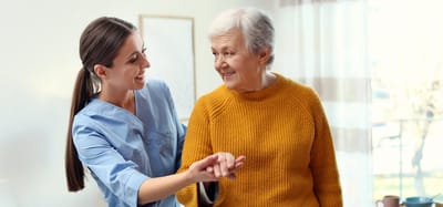 Caregiver assisting an elderly woman with a warm smile.