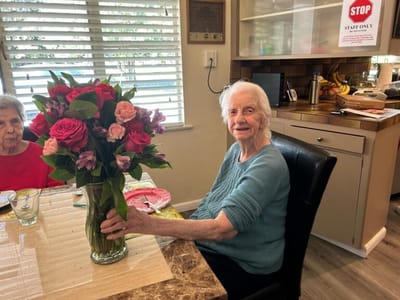 Resident smiling with a bouquet of flowers at a table