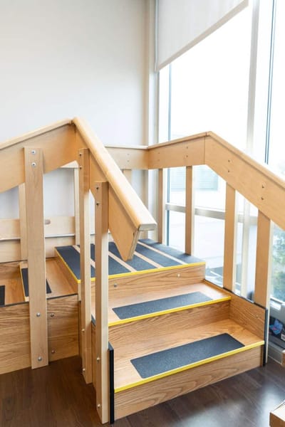 Interior view of stairs with wooden railing and contrast strips