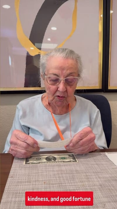 An elderly woman reading a note at a table