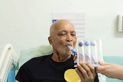 Older man using a spirometer with assistance