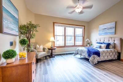 Brightly lit bedroom with a bed, chair, and decorative plants