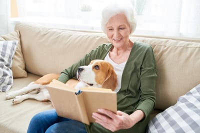 Senior woman reading a book with a dog on her lap