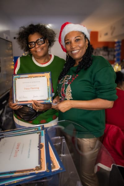 Two women celebrating with certificates in a festive setting.