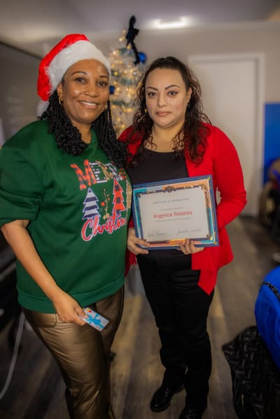 Two women celebrate with a certificate at a holiday event.