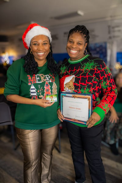 Two women celebrating with a certificate and festive attire.